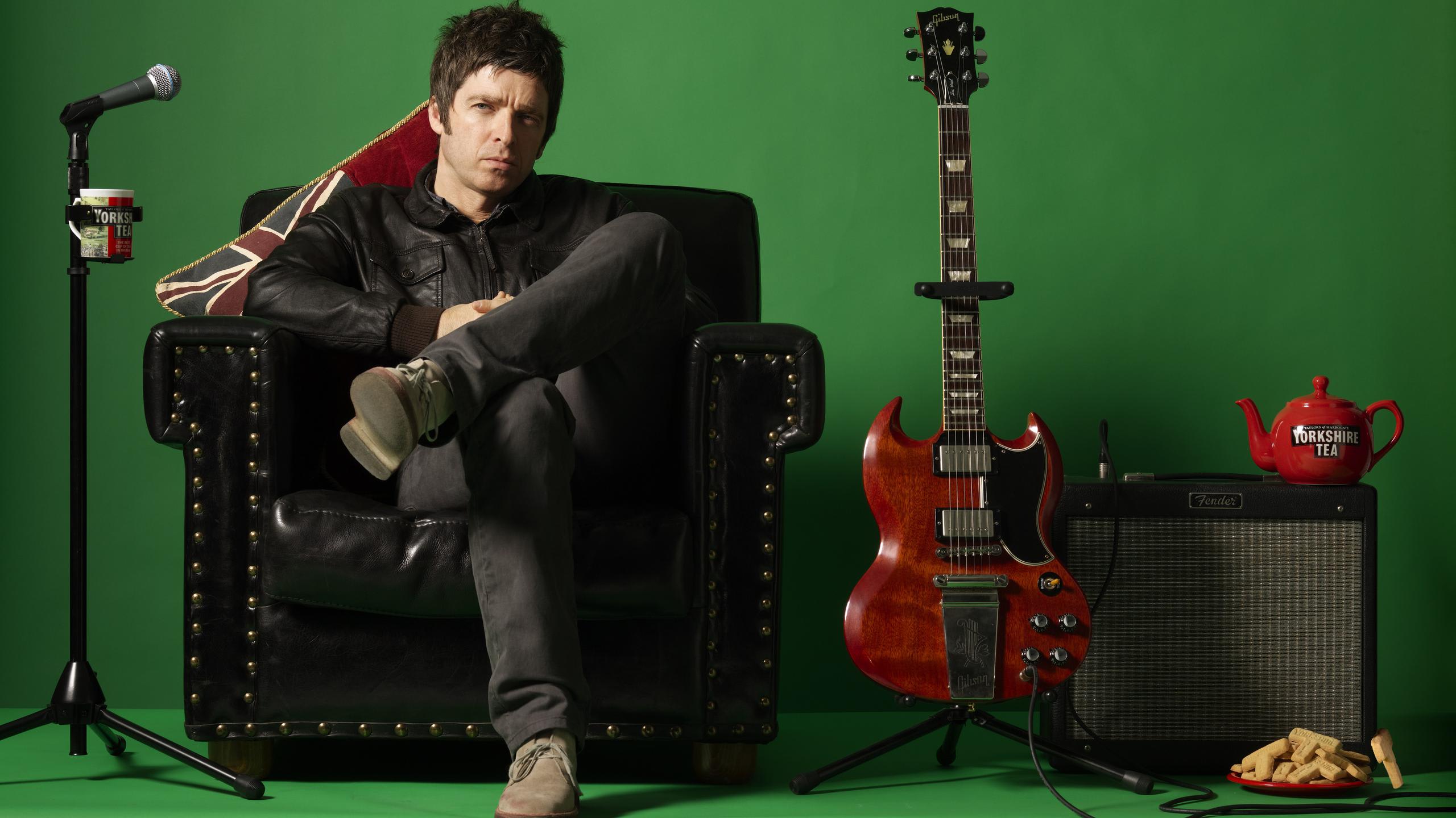 Noel Gallagher sits on a chair beside his guitar