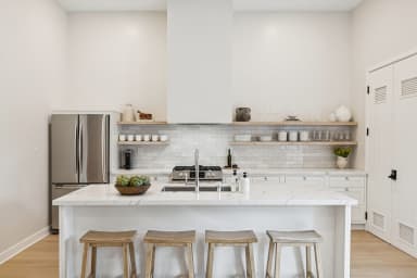 Modern kitchen with a white island, bar seating, and open shelving