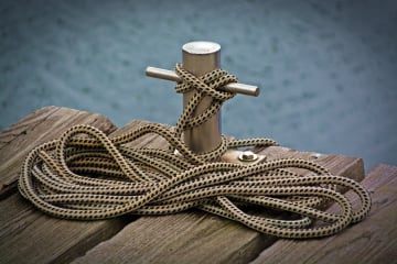 Close-up view of a rope tied to a cleat on a wooden dock over water