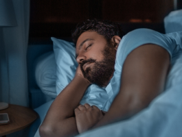 Erwachsener Mann schläft nachts ruhig im Bett in abgedunkeltem Schlafzimmer, Seitenlage mit Kissen – Symbolbild für erholsamen Schlaf, Schlafrhythmus und verändertes Schlafverhalten im Erwachsenenalter.