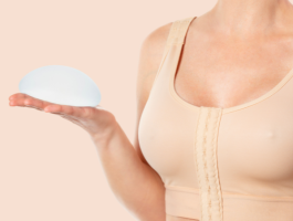 Frau im medizinischen Kompressions-BH hält zwei Silikon-Brustimplantate in den Händen – Symbolbild für Beratung, Implantatauswahl und Vorbereitung auf eine Brustvergrößerung in der ästhetischen Chirurgie