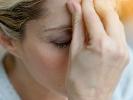 Nahaufnahme einer Frau, die Kopfschmerzen hat und die Hand gegen die Stirn presst.