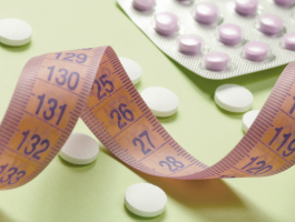 Orangefarbenes Maßband zwischen weißen und violetten Tabletten auf hellgrünem Hintergrund als Symbol für GLP-1-Abnehmtabletten und Gewichtsreduktion.