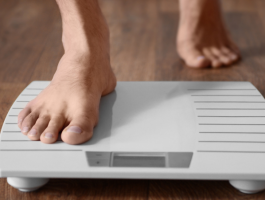 Barfüßige Person steigt auf eine digitale Personenwaage auf einem Holzboden – Symbolbild für schnellen Gewichtsverlust und die Kontrolle des Körpergewichts.