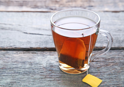 Ein Glas heißer Tee mit einem Teebeutel und einem gelben Etikett, das aus dem Glas hängt. Das Glas steht auf einem rustikalen Holztisch.