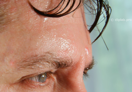 Nahaufnahme einer verschwitzten Stirn und Augenpartie eines Mannes mit nassen Haaren, die an der Stirn kleben.