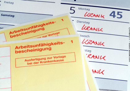 Zwei gelbe "Arbeitsunfähigkeitsbescheinigungen" zur Vorlage bei der Krankenkasse liegen auf einem Kalender. Im Kalender ist in mehreren Tagen hintereinander mit roter Schrift das Wort "KRANK" notiert.
