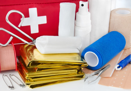 Nahaufnahme eines Erste-Hilfe-Sets mit verschiedenen medizinischen Utensilien, einschließlich einer Schere, einer Pinzette, Verbandmaterial, Pflastern, Sicherheitsnadeln, einer Rettungsdecke und einer Sprühflasche.