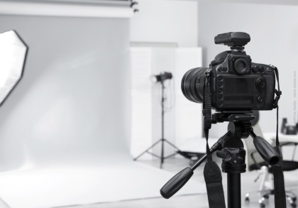 Eine Spiegelreflexkamera steht auf einem Stativ in einem professionellen Fotostudio. Im Hintergrund sind ein weißer Hintergrund, Studiobeleuchtung und weitere Fotoausrüstung zu sehen.