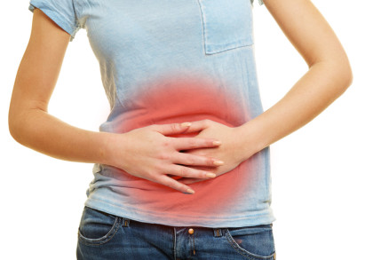 Eine Person hält ihren Bauch mit beiden Händen fest. Der Bereich um den Bauch ist rot überlagert, was auf Schmerzen oder Beschwerden in diesem Bereich hinweist. Die Person trägt ein hellblaues T-Shirt und eine Jeans.