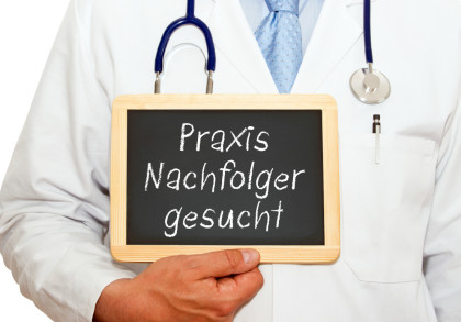 Ein Arzt im weißen Kittel mit Stethoskop hält eine kleine Tafel, auf der "Praxis Nachfolger gesucht" steht.