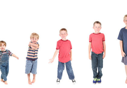 Fünf Jungen unterschiedlicher Altersstufen stehen in einer Reihe vor einem weißen Hintergrund. Von links nach rechts sind die Jungen in aufsteigender Größe und Altersstemmen aufgereiht.
