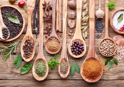 Eine Auswahl verschiedener Gewürze und Kräuter, die sich in Holzlöffeln und -schalen auf einem rustikalen Holztisch befinden.