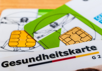 Nahaufnahme von mehreren deutschen Gesundheitskarten (eGK) mit Chiptechnik, auf einem Holztisch liegend. Eine Karte zeigt den Schriftzug "Gesundheitskarte".