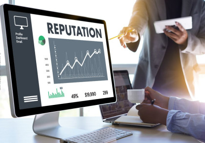 Ein Computerbildschirm zeigt ein Diagramm mit dem Titel "REPUTATION". Es gibt eine Grafik mit ansteigender Kurve und Kennzahlen darunter. Eine Person mit einem Stift deutet auf den Bildschirm, während eine andere eine Tasse und ein Notebook hält.