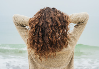 Blick aufs Meer. Frau von hinten mit braunen Locken.