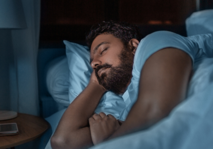 Erwachsener Mann schläft nachts ruhig im Bett in abgedunkeltem Schlafzimmer, Seitenlage mit Kissen – Symbolbild für erholsamen Schlaf, Schlafrhythmus und verändertes Schlafverhalten im Erwachsenenalter.