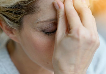 Nahaufnahme einer Frau, die Kopfschmerzen hat und die Hand gegen die Stirn presst.