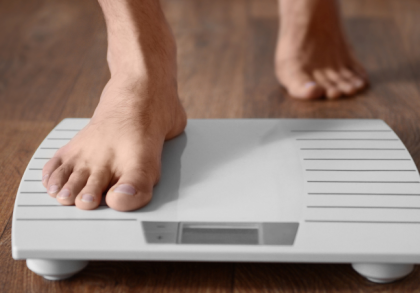 Barfüßige Person steigt auf eine digitale Personenwaage auf einem Holzboden – Symbolbild für schnellen Gewichtsverlust und die Kontrolle des Körpergewichts.
