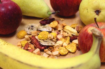 Verschiedene frische Früchte, darunter Äpfel, Birnen und Bananen, umgeben eine Mischung aus getrockneten Obststücken auf einem Holzbrett.