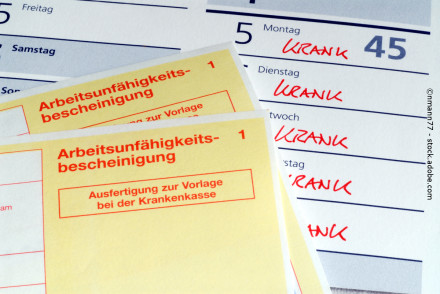 Zwei gelbe "Arbeitsunfähigkeitsbescheinigungen" zur Vorlage bei der Krankenkasse liegen auf einem Kalender. Im Kalender ist in mehreren Tagen hintereinander mit roter Schrift das Wort "KRANK" notiert.