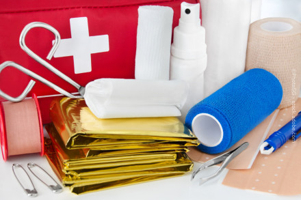 Nahaufnahme eines Erste-Hilfe-Sets mit verschiedenen medizinischen Utensilien, einschließlich einer Schere, einer Pinzette, Verbandmaterial, Pflastern, Sicherheitsnadeln, einer Rettungsdecke und einer Sprühflasche.