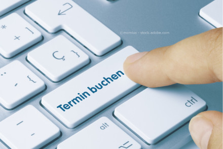 Eine Nahaufnahme einer Computer-Tastatur mit einer Taste beschriftet als "Termin buchen". Ein Finger drückt diese Taste.