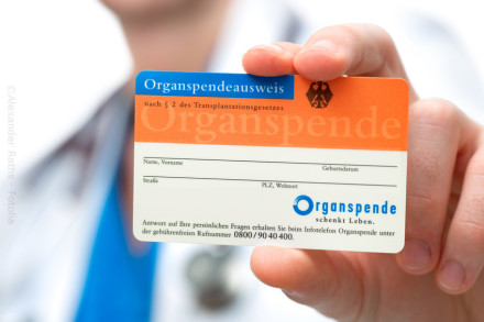 Ein Hand hält einen deutschen Organspendeausweis. Der Ausweis ist orange und blau und hat Felder für Name, Vorname, Geburtsdatum, Straße, Postleitzahl und Wohnort. Oben steht "Organspendeausweis nach § 2 des Transplantationsgesetzes".