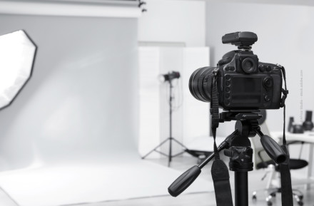 Eine Spiegelreflexkamera steht auf einem Stativ in einem professionellen Fotostudio. Im Hintergrund sind ein weißer Hintergrund, Studiobeleuchtung und weitere Fotoausrüstung zu sehen.