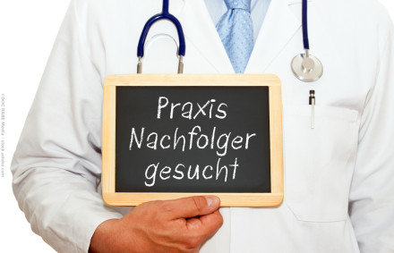Ein Arzt im weißen Kittel mit Stethoskop hält eine kleine Tafel, auf der "Praxis Nachfolger gesucht" steht.