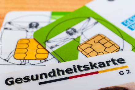 Nahaufnahme von mehreren deutschen Gesundheitskarten (eGK) mit Chiptechnik, auf einem Holztisch liegend. Eine Karte zeigt den Schriftzug "Gesundheitskarte".