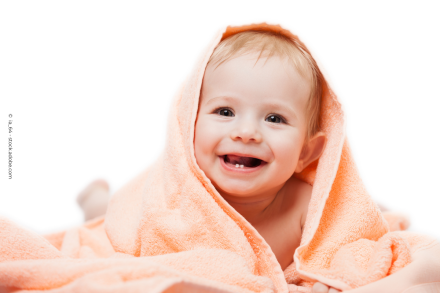 Ein lächelndes Baby, das in ein orangefarbenes Handtuch eingewickelt ist.