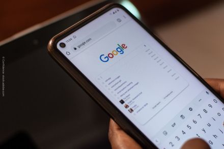 Nahaufnahme eines Smartphones, auf dem die Google-Suchseite geöffnet ist. Die Person gibt gerade eine Suchanfrage ein. Man sieht das Google-Logo oben auf dem Bildschirm und einige Suchvorschläge darunter. Der Hintergrund ist verschwommen.
