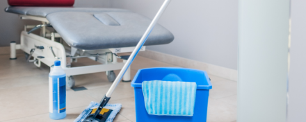 Ein sauberer Behandlungsraum in einer Arztpraxis mit Wischmopp, Eimer und Reinigungsmittel, die auf hygienische Sauberkeit und Infektionsprävention hinweisen.