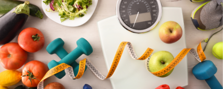Eine Waage, ein Maßband, Hanteln und Sportschuhe, die für Bewegung und Fitness stehen. Es ist frisches Obst, Gemüse, Salat und eine Wasserflasche zu sehen, die eine ausgewogene Ernährung und ausreichende Flüssigkeitszufuhr symbolisieren.