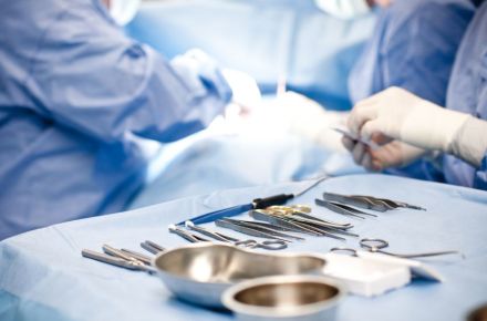 Steril angeordnete chirurgische Instrumente wie Scheren, Pinzetten und Klemmen auf einem blauen OP-Tuch, mit unscharfen Chirurgen im Hintergrund, die an einem Eingriff arbeiten. Darstellung einer professionellen OP-Umgebung.