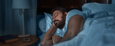 Erwachsener Mann schläft nachts ruhig im Bett in abgedunkeltem Schlafzimmer, Seitenlage mit Kissen – Symbolbild für erholsamen Schlaf, Schlafrhythmus und verändertes Schlafverhalten im Erwachsenenalter.