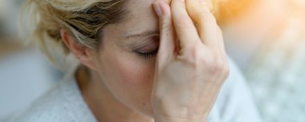 Nahaufnahme einer Frau, die Kopfschmerzen hat und die Hand gegen die Stirn presst.
