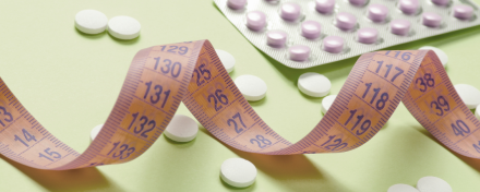 Orangefarbenes Maßband zwischen weißen und violetten Tabletten auf hellgrünem Hintergrund als Symbol für GLP-1-Abnehmtabletten und Gewichtsreduktion.