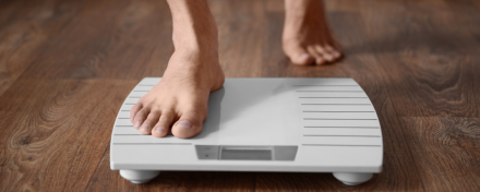Barfüßige Person steigt auf eine digitale Personenwaage auf einem Holzboden – Symbolbild für schnellen Gewichtsverlust und die Kontrolle des Körpergewichts.