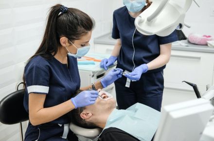 Eine Zahnärztin behandelt einen Patienten. Dieser liegt auf dem Zahnarztstuhl und hat den Mund weit geöffnet.