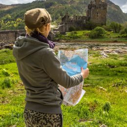Young woman tourist looks at a road map. In background the famous and spectacular Eilean Donan Castle in Dornie, Kyle of Lochalsh, Scotland, United Kingdom