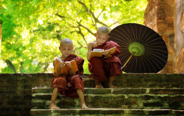 Zwei junge buddhistische Mönche in Myanmar lesen auf der Treppe eines Klosters sitzend