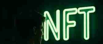A person in shadow stands facing a glowing green neon sign that reads "NFT" against a dark background.