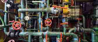 A complex network of green pipes, valves, and gauges in an industrial setting with numerous red-handled controls and a yellow tank. The pipes are interconnected in various configurations, indicating a possibly large and intricate system.