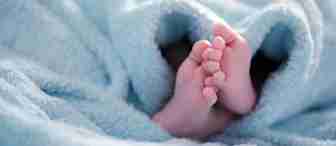 Close-up of a baby's feet peeking out from under a soft, light blue blanket. The blanket appears fluffy and cozy, enveloping the baby in warmth. The baby's tiny toes are slightly splayed, highlighting their delicate nature against the plush fabric.