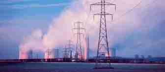 Power lines stretch across a field towards a power plant with cooling towers emitting white steam against a blue sky. The scene is illuminated by the soft pink and purple hues of either sunrise or sunset, contrasting with the industrial structures.