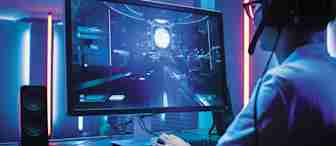 A person wearing glasses and headphones is sitting at a desk, playing a futuristic video game on a large monitor. The room is illuminated with blue and pink neon lights, and speakers are placed on both sides of the monitor.
