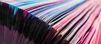 Close-up of a book with colorful pages fanned out. The edges of the pages display a spectrum of vibrant colors ranging from pink to blue, creating a striking and visually appealing pattern.