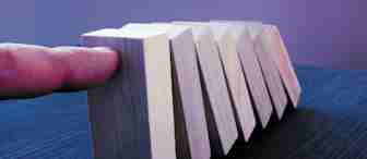 A finger is pushing the first of several aligned wooden domino blocks on a dark surface, causing a chain reaction. The dominoes are all in different stages of falling, illustrating the domino effect concept. The background is a gradient of blue and purple shades.